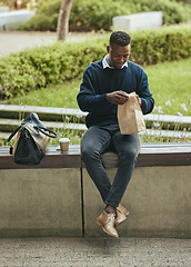 Image showing Business man eating food for lunch on his break outdoors at a park opening a brown paper bag. Hungry, happy black male time to eat and drink outside in the city. Enjoying a takeaway or takeout meal