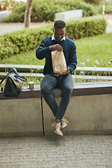 Image showing Black business man on a lunch break in the city, sitting and eating a meal or sandwich in a brown paper bag. Hungry worker relaxing with a tasty snack, food on the go for a professional entrepreneur