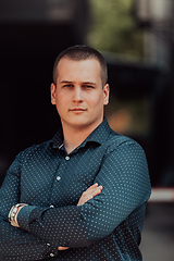 Image showing A successful young businessman in a shirt, with crossed arms, poses outdoors, confident expression on his face.