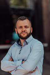 Image showing A successful young businessman in a shirt, with crossed arms, poses outdoors, confident expression on his face.