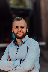 Image showing A successful young businessman in a shirt, with crossed arms, poses outdoors, confident expression on his face.