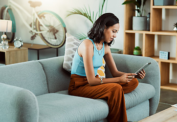 Image showing Browsing for movies to watch online on a tablet, streaming videos and scrolling on social media while relaxing on the couch alone at home. Stylish, trendy and casual female browsing the internet