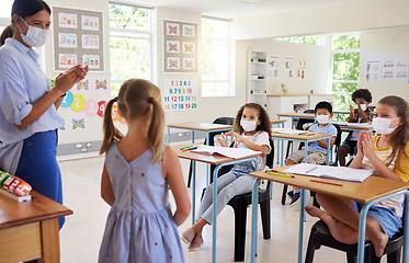 Image showing Covid, education and learning with a teacher wearing a mask and clapping for a student after her oral with classmates in class during school. Young girl talking or sharing her answer in a classroom