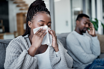 Image showing Young, sick and ill woman blowing her nose with tissues while sitting on the couch at home. African lady has cold or flu and needs medicine. Husband worried about wife suffering from illness