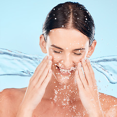 Image showing Woman, face and skincare with splash in studio for beauty, wellness and self care by blue background. Water, model and smile with moisturizer, cleaning and happy for natural cosmetics for dermatology