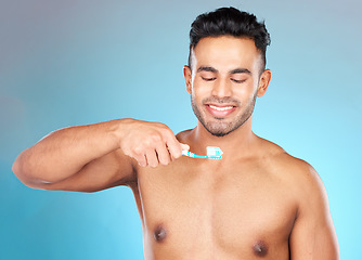 Image showing Teeth, dental care and man brushing teeth with toothbrush and toothpaste on blue background with smile on face. Morning routine, healthcare and fresh, happy male model from India in studio portrait.