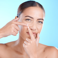 Image showing Skincare, portrait and woman squeeze a pimple in a studio for a natural facial treatment. Beauty, cosmetic and girl model from brazil with a face acne routine for health isolated by a blue background