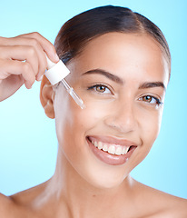 Image showing Woman, facial skincare and serum in studio on a blue background to promote a cosmetic product. Face smile, beauty and antiaging with a happy female applying oil to her skin for natural cosmetology