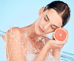 Image showing Beauty, splash and water with a woman holding fruit for health, skincare and wellness on a blue studio background. Clean, shower and cosmetics with a grapefruit for vitamin c skin care and bodycare