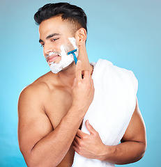 Image showing Man, shaving face and studio for wellness, skincare and towel with happiness by blue background. Model, facial hair removal and cosmetic foam for skin, self care and beauty with cosmetics by backdrop