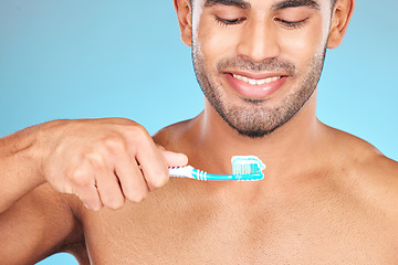 Image showing Toothbrush, toothpaste and man happy brushing teeth for dental care, morning hygiene and cleaning in studio. Smile, tooth whitening and mouth healthcare or oral care happiness in blue background