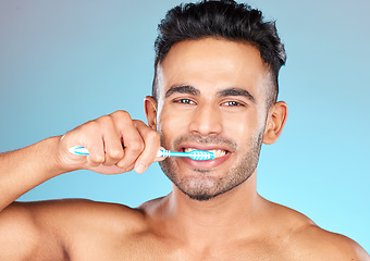 Image showing Face portrait, dental and man brushing teeth in studio isolated on a blue background. Wellness, oral health and routine of happy male model holding toothbrush for hygiene, oral care and dental care.