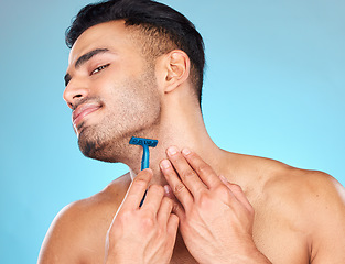 Image showing Man shaving, razor and grooming beard or facial hair for self care, skincare and body wellness on blue studio background. Face of indian model with a smile for clean shave, cosmetics and healthy skin