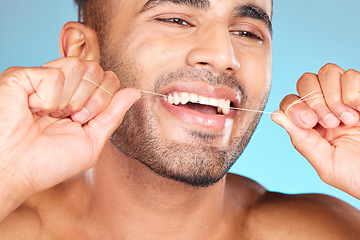 Image showing Face, dental and man floss teeth in studio isolated on blue background. Veneers, invisalign and male model from Brazil flossing, cleaning for wellness or mouth hygiene, oral care and tooth health.