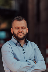 Image showing A successful young businessman in a shirt, with crossed arms, poses outdoors, confident expression on his face.