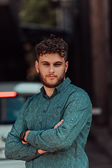 Image showing A successful young businessman in a shirt, with crossed arms, poses outdoors, confident expression on his face.