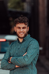 Image showing A successful young businessman in a shirt, with crossed arms, poses outdoors, confident expression on his face.