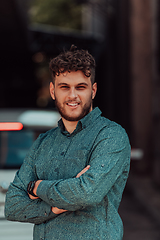 Image showing A successful young businessman in a shirt, with crossed arms, poses outdoors, confident expression on his face.