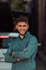 Image showing A successful young businessman in a shirt, with crossed arms, poses outdoors, confident expression on his face.