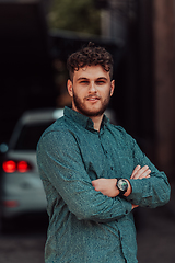 Image showing A successful young businessman in a shirt, with crossed arms, poses outdoors, confident expression on his face.