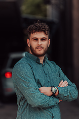 Image showing A successful young businessman in a shirt, with crossed arms, poses outdoors, confident expression on his face.