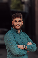 Image showing A successful young businessman in a shirt, with crossed arms, poses outdoors, confident expression on his face.