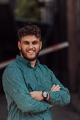 Image showing A successful young businessman in a shirt, with crossed arms, poses outdoors, confident expression on his face.