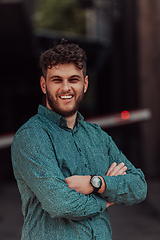 Image showing A successful young businessman in a shirt, with crossed arms, poses outdoors, confident expression on his face.