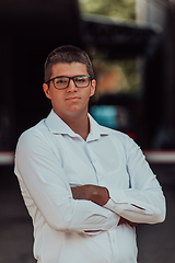 Image showing A successful businessman in a white shirt, with crossed arms, poses outdoors, confident expression on his face.