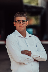 Image showing A successful businessman in a white shirt, with crossed arms, poses outdoors, confident expression on his face.