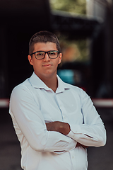 Image showing A successful businessman in a white shirt, with crossed arms, poses outdoors, confident expression on his face.