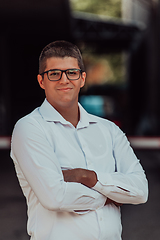 Image showing A successful businessman in a white shirt, with crossed arms, poses outdoors, confident expression on his face.