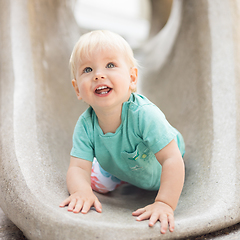 Image showing Child playing on outdoor playground. Toddler plays on school or kindergarten yard. Active kid on stone sculpured slide. Healthy summer activity for children. Little boy climbing outdoors.