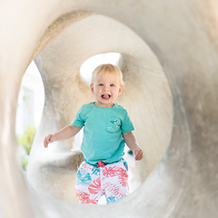 Image showing Child playing on outdoor playground. Toddler plays on school or kindergarten yard. Active kid on stone sculpured slide. Healthy summer activity for children. Little boy climbing outdoors.