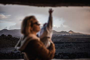 Image showing Mother enjoying winter vacations playing with his infant baby boy son on black sandy volcanic beach of Janubio on Lanzarote island, Spain on windy overcast day. Family travel vacations concept.