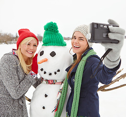 Image showing Selfie, snowman and winter with woman friends taking a photograph outdoor together in the snow. Happy, smile and photography with a young female and friend posing for a picture in the cold weather