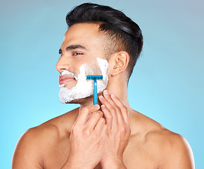 Image showing Studio, skincare and man shaving beard with razor blade for beauty wellness, grooming or self care on blue background. Hair removal, face or model cutting facial hair in morning routine with product