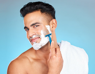 Image showing Man, face and shaving in studio for skincare, wellness and towel in portrait by blue background. Model, facial hair removal and cosmetic cream for skin, self care and cleaning with cosmetics beauty