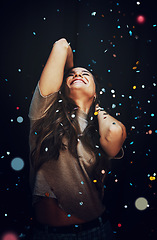 Image showing Party, confetti and celebration with a woman in studio on a dark background for a new year event. Birthday, energy and smile with a happy young female on a black backdrop for a nightlife social