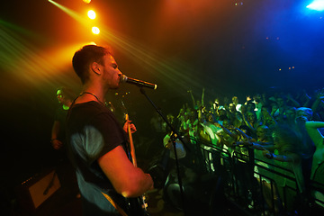 Image showing Concert, band and music with a man guitarist playing at a gig for a crowd or audience at a performance event. Festival, stage and social with a male artist strumming a guitar while singing at a show