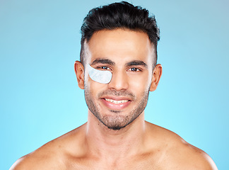 Image showing Portrait, face and eye mask with a man model in studio on a blue background for antiaging skincare. Product, wellness and beauty with a handsome young male using cosmetic treatment for dermatology