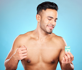 Image showing Man, body or dental floss for grooming, mouth hygiene maintenance or plaque removal help on blue background in studio. Smile, happy or flossing model and teeth product in healthcare wellness cleaning