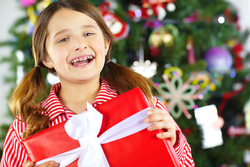 Image showing Christmas, gift box and excited child with present ready to celebrate holiday, vacation and festival tradition. Happiness, festive celebration and face of girl with braces with gift by Christmas tree
