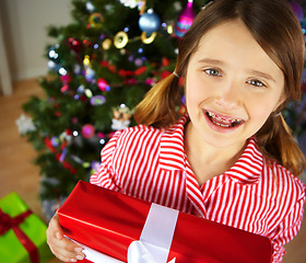 Image showing Christmas, girl and gift for celebration, excited and festive season. Portrait, braces and female child enjoy presents, happiness and vacation for Xmas, break and holiday to relax, joy and in lounge