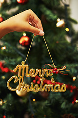 Image showing Merry Christmas sign, hand of woman and decoration for Christmas tree in home. Xmas, holiday or vacation and female holding golden ornaments or decorations for festive party or celebration in house.