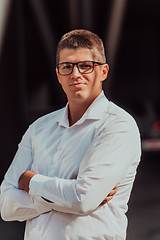 Image showing A successful businessman in a white shirt, with crossed arms, poses outdoors, confident expression on his face.