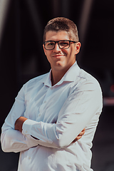 Image showing A successful businessman in a white shirt, with crossed arms, poses outdoors, confident expression on his face.