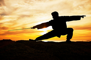 Image showing Sunset, sport and man doing tai chi with a sword on a hill for exercise and fitness workout. Silhouette, training and sports exercising male at sunrise for chi gong practice for health and wellness