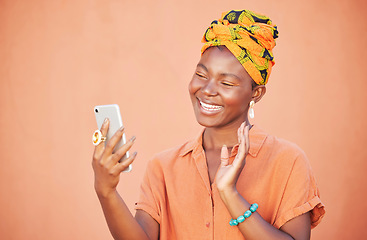 Image showing Black woman, phone and video call, wave and communication outdoor against peach wall outdoor. Girl, fashion and virtual conversation, video conference and happy smile or talking with smartphone