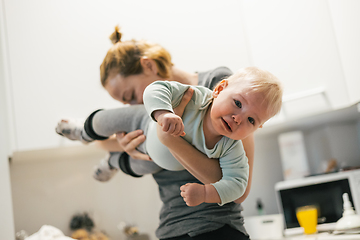 Image showing That awkward moment when your mom sniffs your butt. Mother holding her baby, sniffing stinky diaper of her little boy checking if it is time to change it.